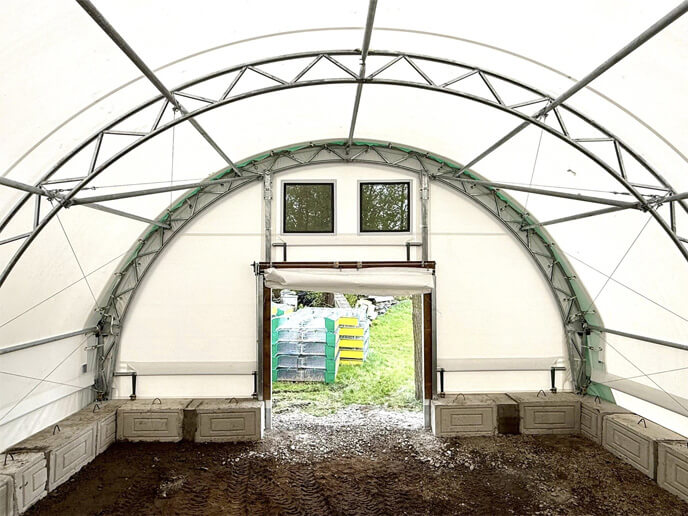 Intérieur d’un bâtiment en toile avec charpente d’acier galvanisé et porte ouverte donnant sur l’extérieur